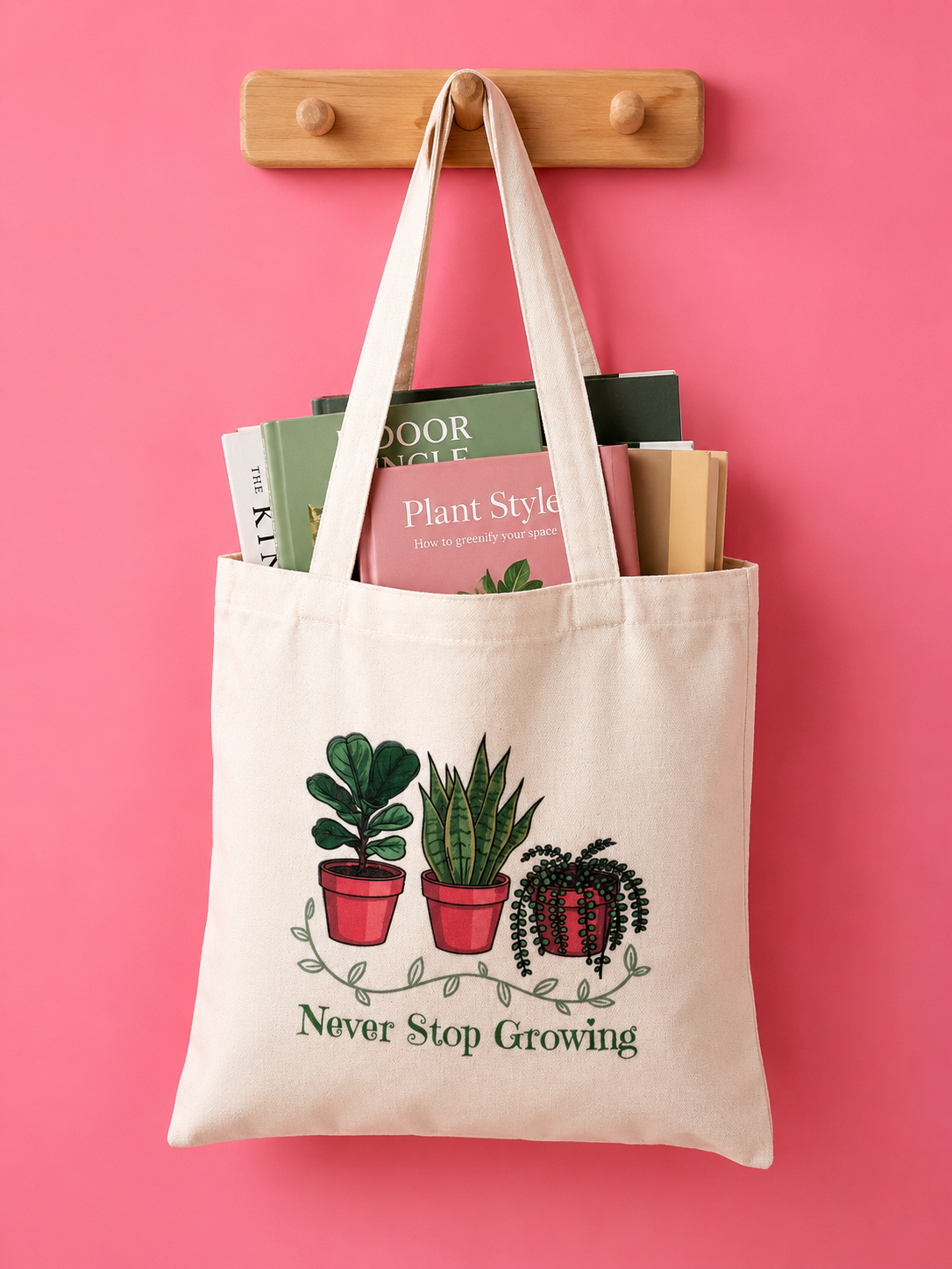 Vit tygväska med illustrerade krukväxter och texten Never Stop Growing hängande på träkrok mot rosa bakgrund